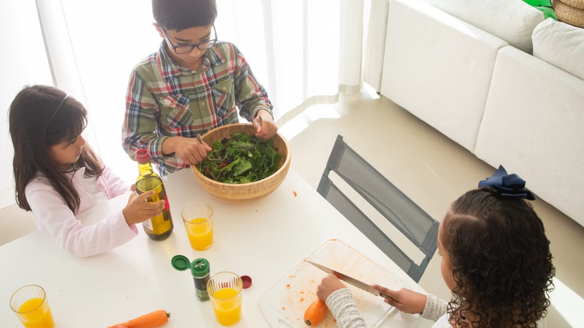 Three children preparing a healthy salad in a bright kitchen setting.
